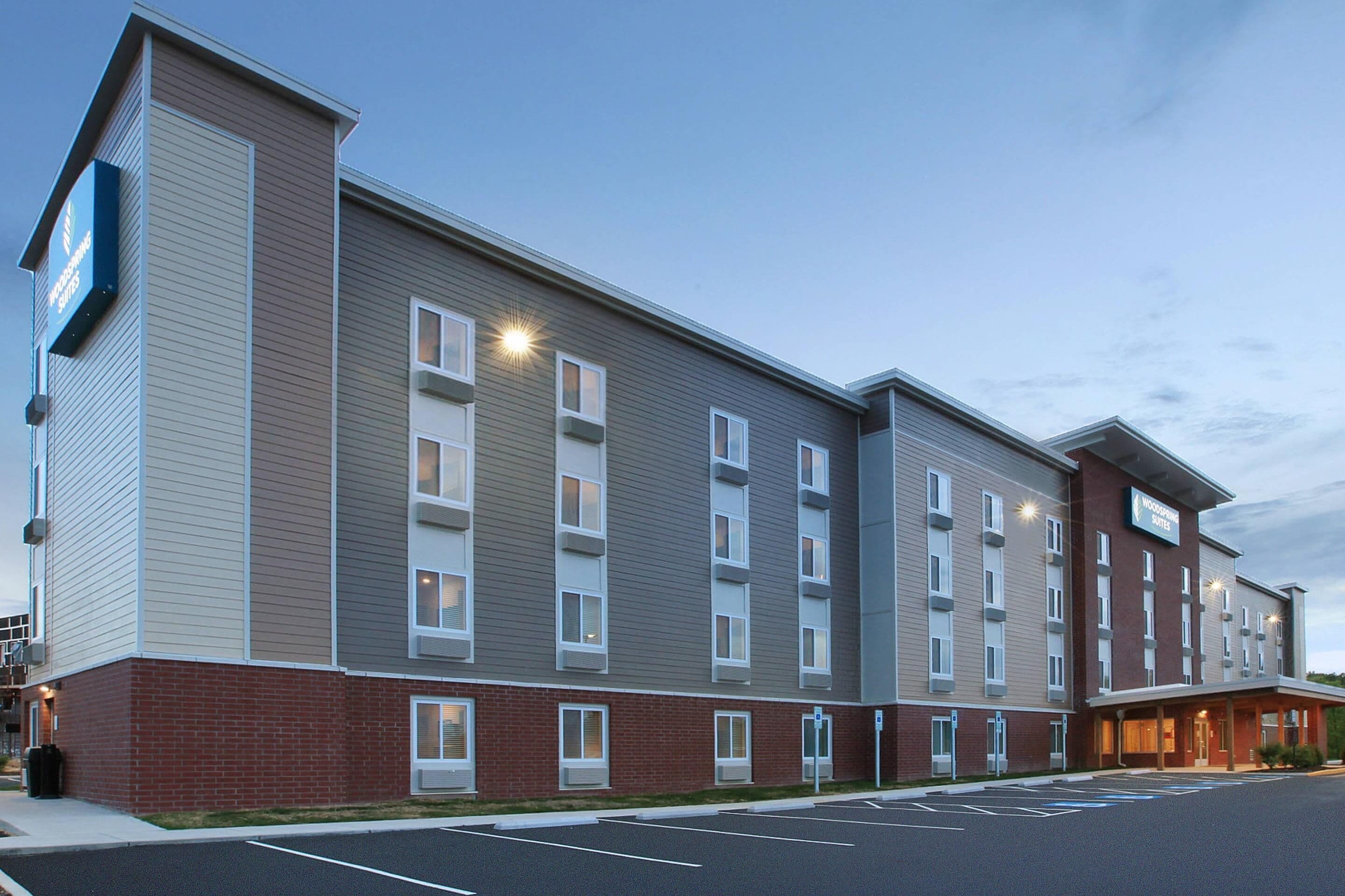 A multi-story hotel building with a flat roof, large windows, and a parking lot in front.