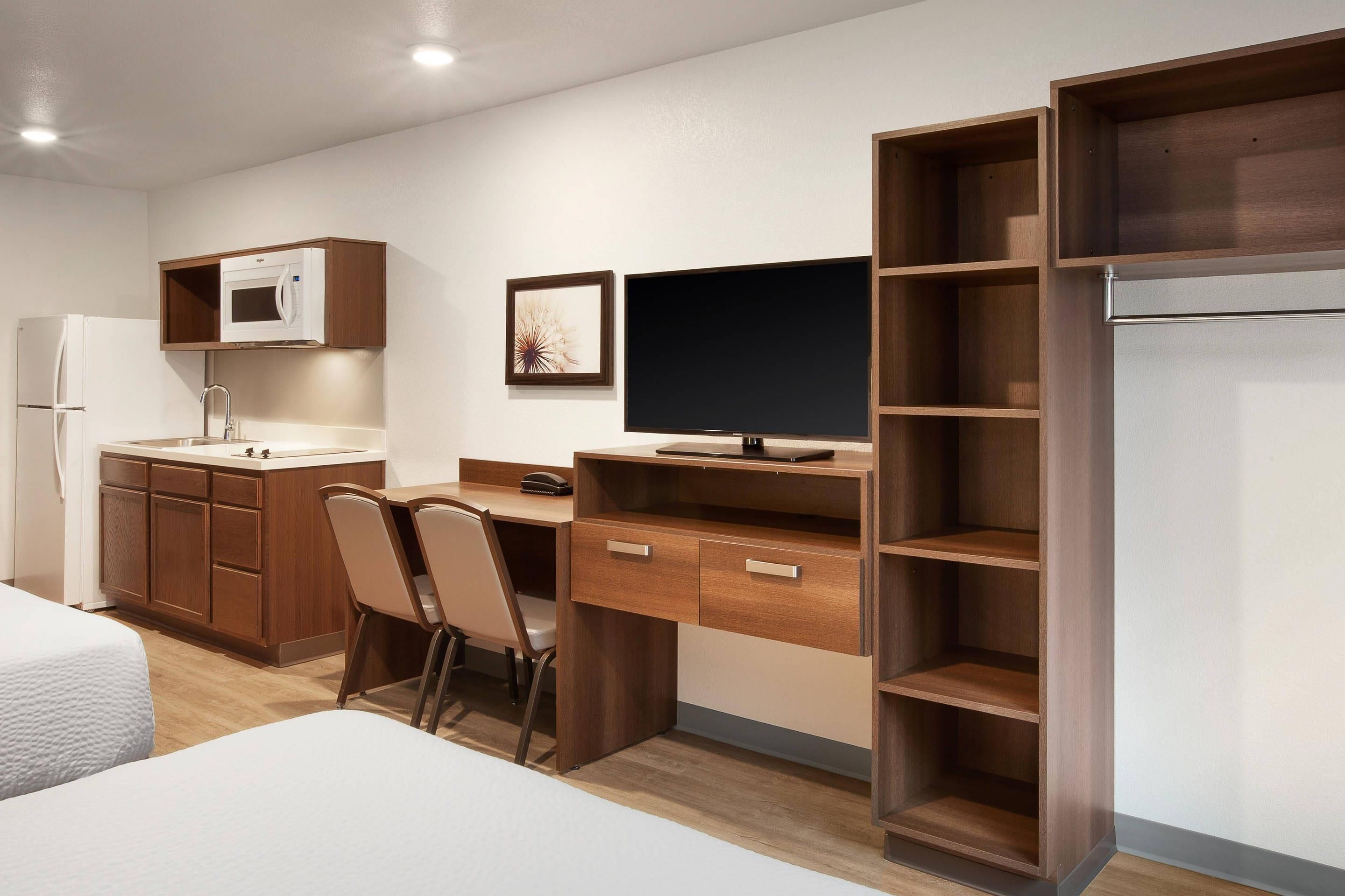 Habitación de hotel pequeña con kitchenette, una cama, un escritorio con silla y un televisor.