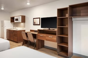 Habitación de hotel pequeña con kitchenette, una cama, un escritorio con silla y un televisor.