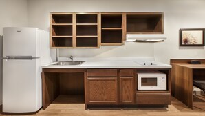 A compact kitchen with a built-in refrigerator, microwave, and wooden cabinets. - WoodSpring Suites Quantico (Stafford)
