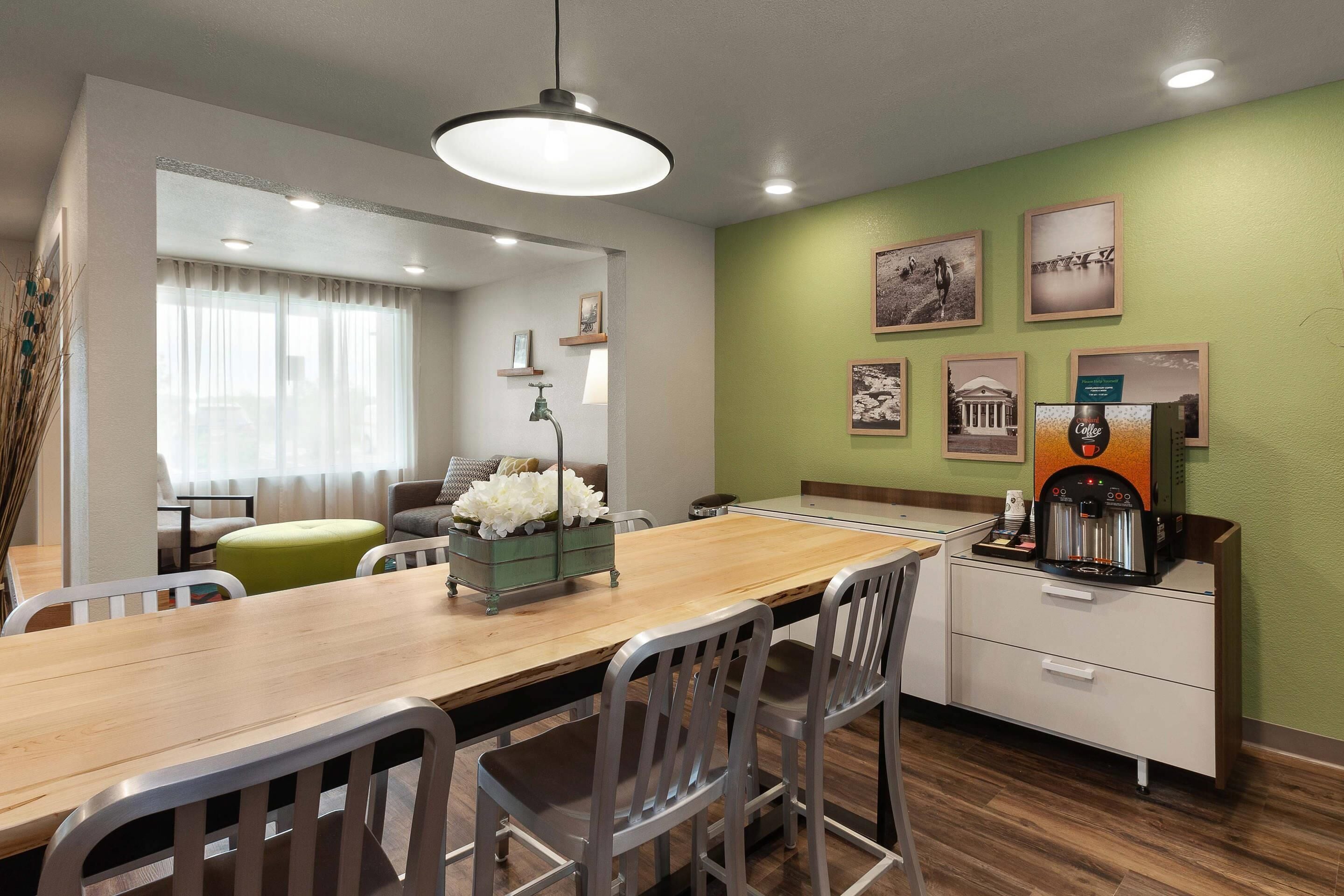 A dining area with a wooden table, metal chairs, a coffee machine, and framed pictures on the wall.