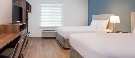 Quarto de hotel com duas camas, uma escrivaninha com televisão, uma janela com persianas e uma luminária.