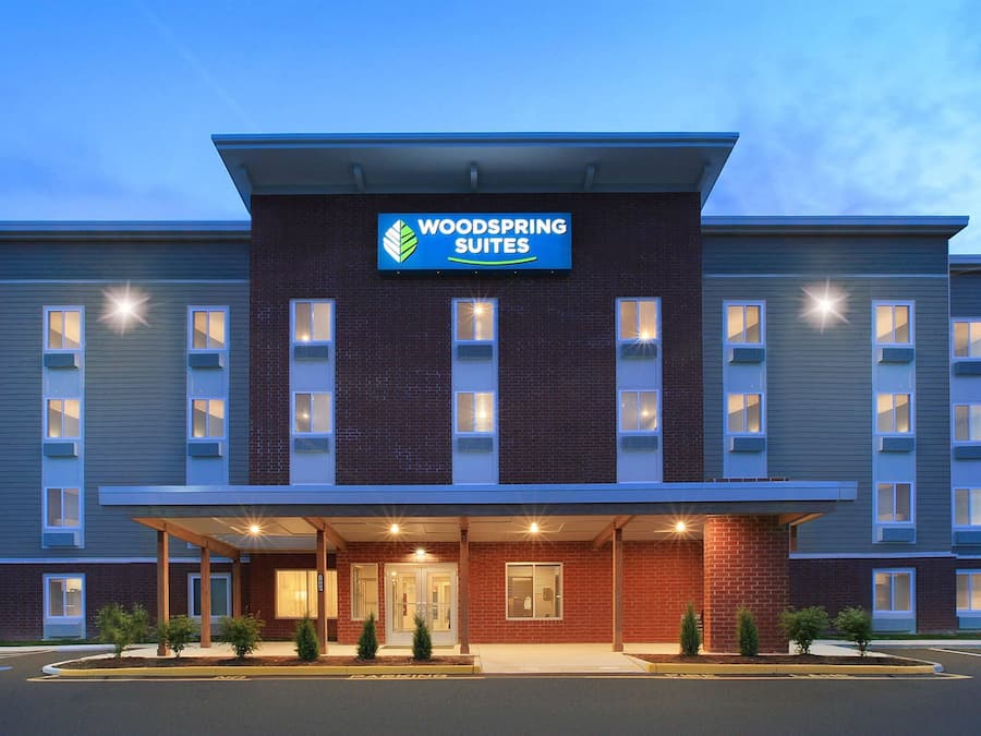 A hotel with a sign reading 'WOODS SPRING SUITES' and a covered entrance with a brick facade.