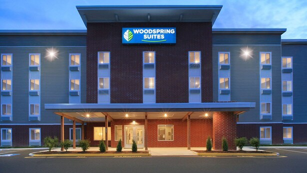 Et hotel med et skilt, der viser "Woodspring Suites", og en overdækket indgang med murstensfacade.