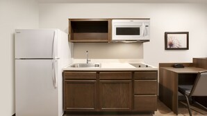 A compact kitchen with a white refrigerator, a microwave, and wooden cabinets. - WoodSpring Suites Quantico (Stafford)