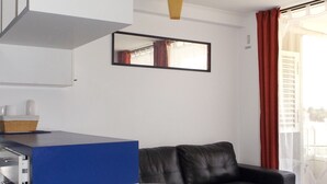 A modern living room with a black leather sofa, a white round dining table with matching chairs, a blue accent wall, and a large mirror. - Playa Blanca (La Serena)