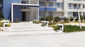 A modern multi-story building with a prominent blue facade, a central entrance, and a landscaped area with benches and plants. - Playa Blanca (La Serena)