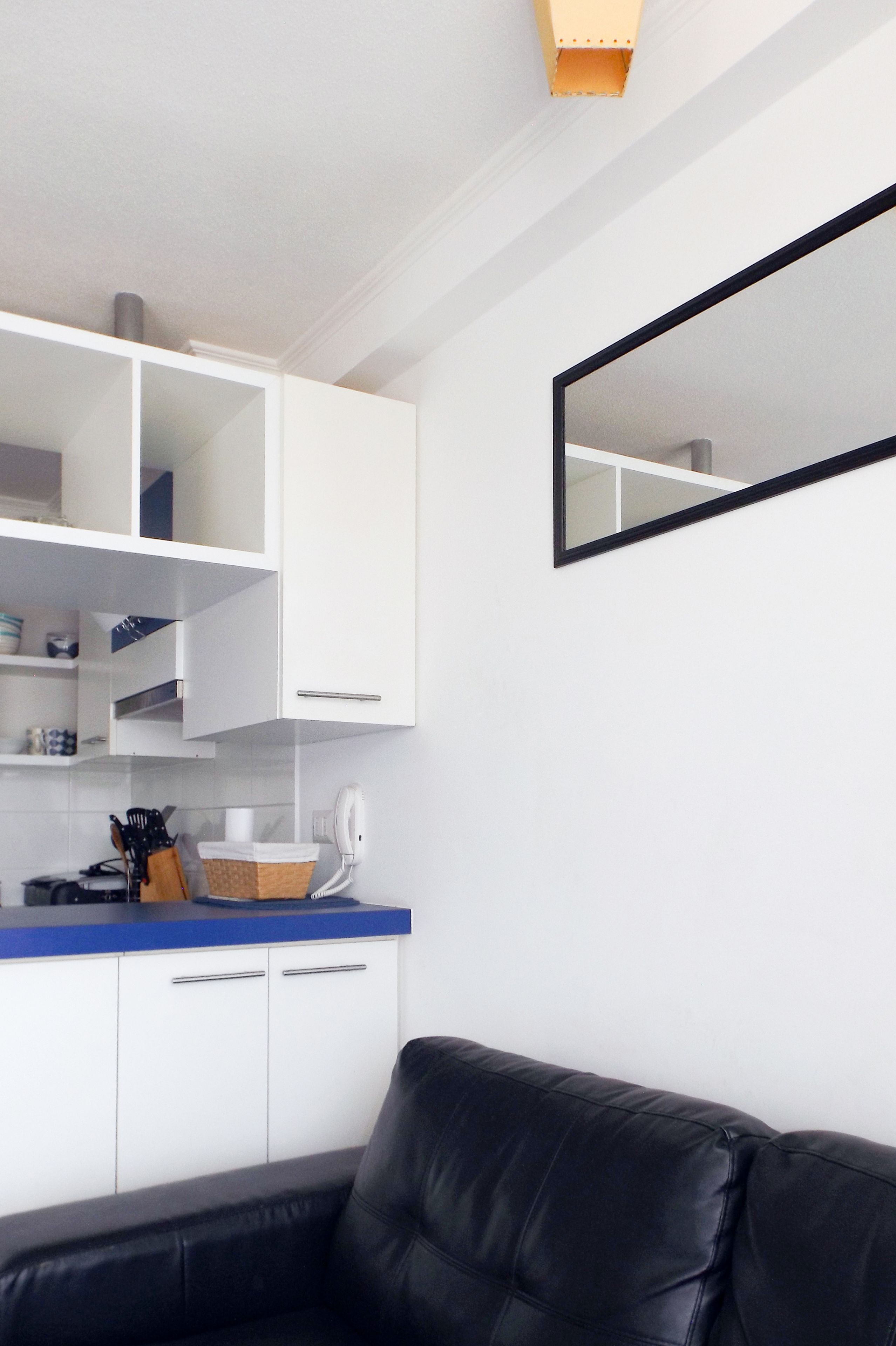 Cozinha moderna com armários brancos, bancada azul e sofá de couro preto.