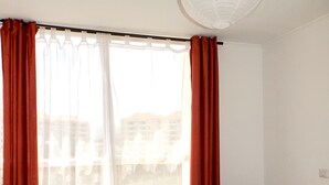 A bedroom with a bed, a nightstand, a chair, and a window with curtains. - Playa Blanca (La Serena)