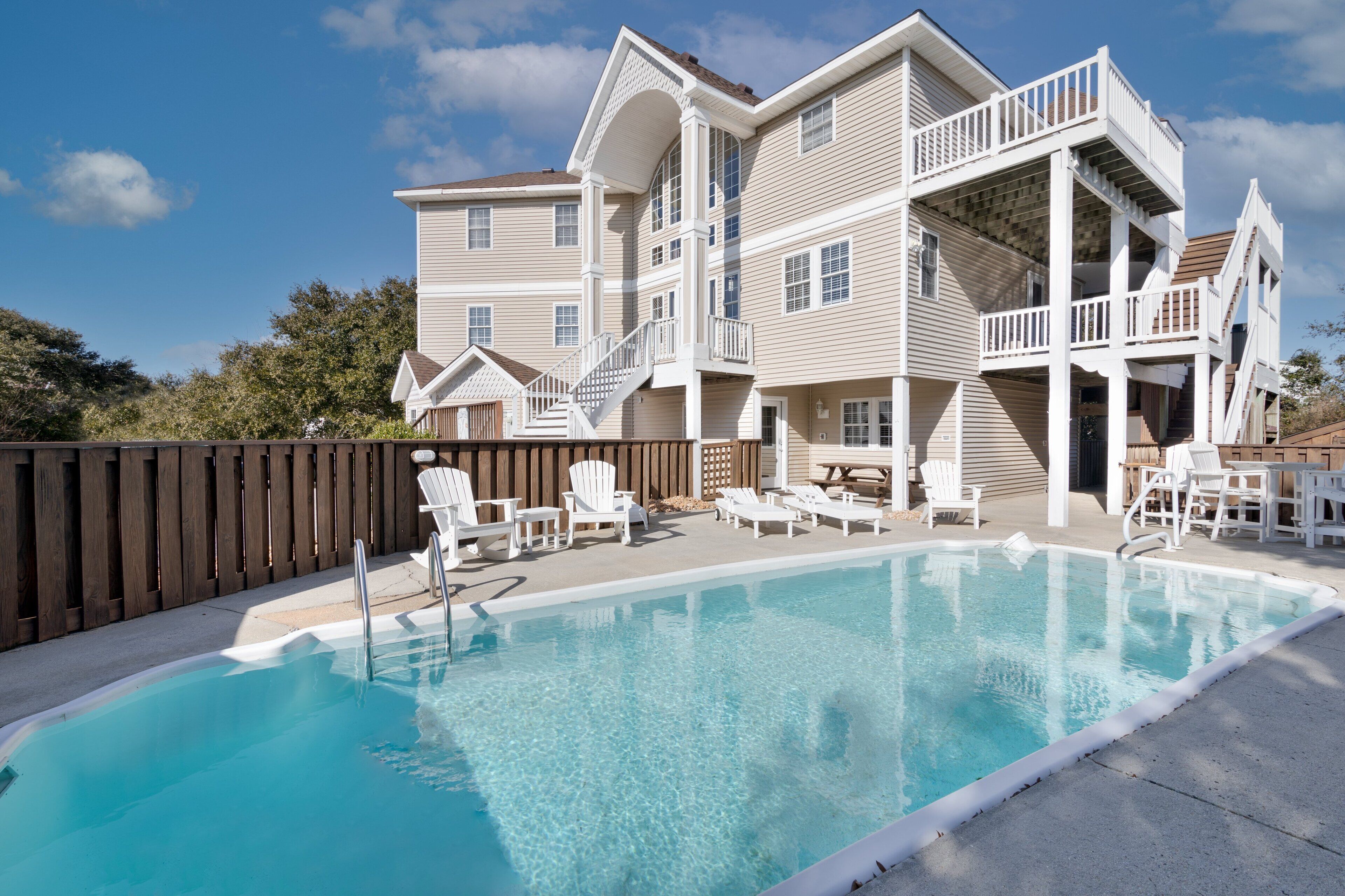 A two-story building with a swimming pool, outdoor seating, and a wooden deck.