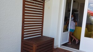 Eine Holzbank mit horizontalen Lamellen, ein mit Fliesen ausgelegter Patio und eine Tür zu einem Zimmer.