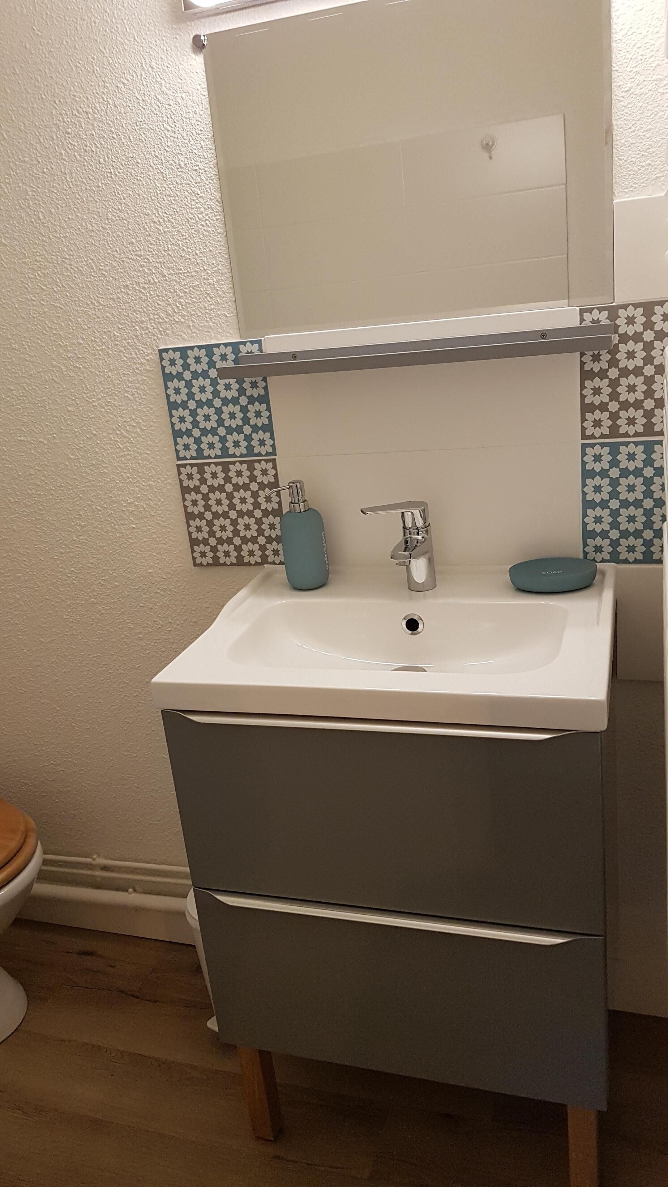 A bathroom with a white sink, a mirror above it, and patterned tiles on the walls.