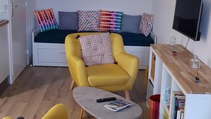 Ein gemütlicher Wohnbereich mit einer Couch, zwei Sesseln, einem kleinen Couchtisch, einem Fernseher und einem Bücherregal.