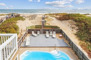 Relax on the beachfront deck with lounge chairs and a table, overlooking the ocean and pool.