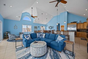 Uma sala de estar ampla, com um sofá azul, uma mesa de centro redonda e uma área de jantar com cadeiras de madeira.