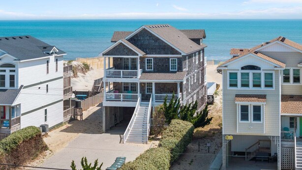 A beachfront property with multiple buildings, including a two-story house with a balcony and a covered walkway. - 5849- Mari-Time, Oceanfront 8BR Luxury: Theater, Pool & Elevator (South Nags Head)