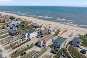 Vue aérienne d’une zone résidentielle côtière, avec des maisons, une plage et une jetée.