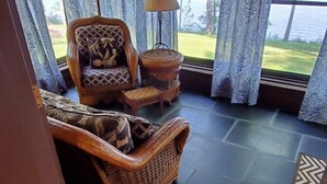 Une pièce dotée d’une grande fenêtre, d’un canapé en osier, d’une petite table ronde avec une lampe et d’un tapis à motifs.