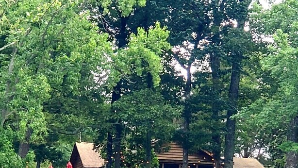Une cabane dotée d’une terrasse, entourée d’arbres et bordée par un plan d’eau.