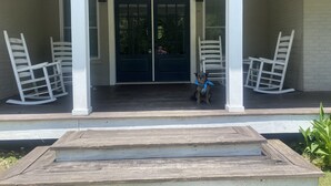 Une véranda avec des fauteuils à bascule blancs et un chien portant un bandana bleu.
