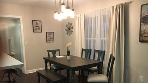 Un coin repas avec une table en bois foncé, six chaises et un banc. Deux luminaires sont fixés au mur au-dessus de la table.