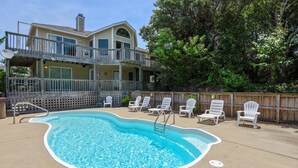 A swimming pool with a wooden deck, lounge chairs, and a two-story building with balconies. - 1537 - Carolina Sunset - Soundside Sunsets w/ Pool, Hot Tub & Game Room (Corolla)