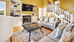 A living room with a sofa, a coffee table, a fireplace, and a TV. - 1537 - Carolina Sunset - Soundside Sunsets w/ Pool, Hot Tub & Game Room (Corolla)