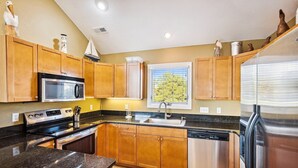 A modern kitchen with wooden cabinets, a stainless steel refrigerator, a microwave, a stove, and a dishwasher. - 1537 - Carolina Sunset - Soundside Sunsets w/ Pool, Hot Tub & Game Room (Corolla)