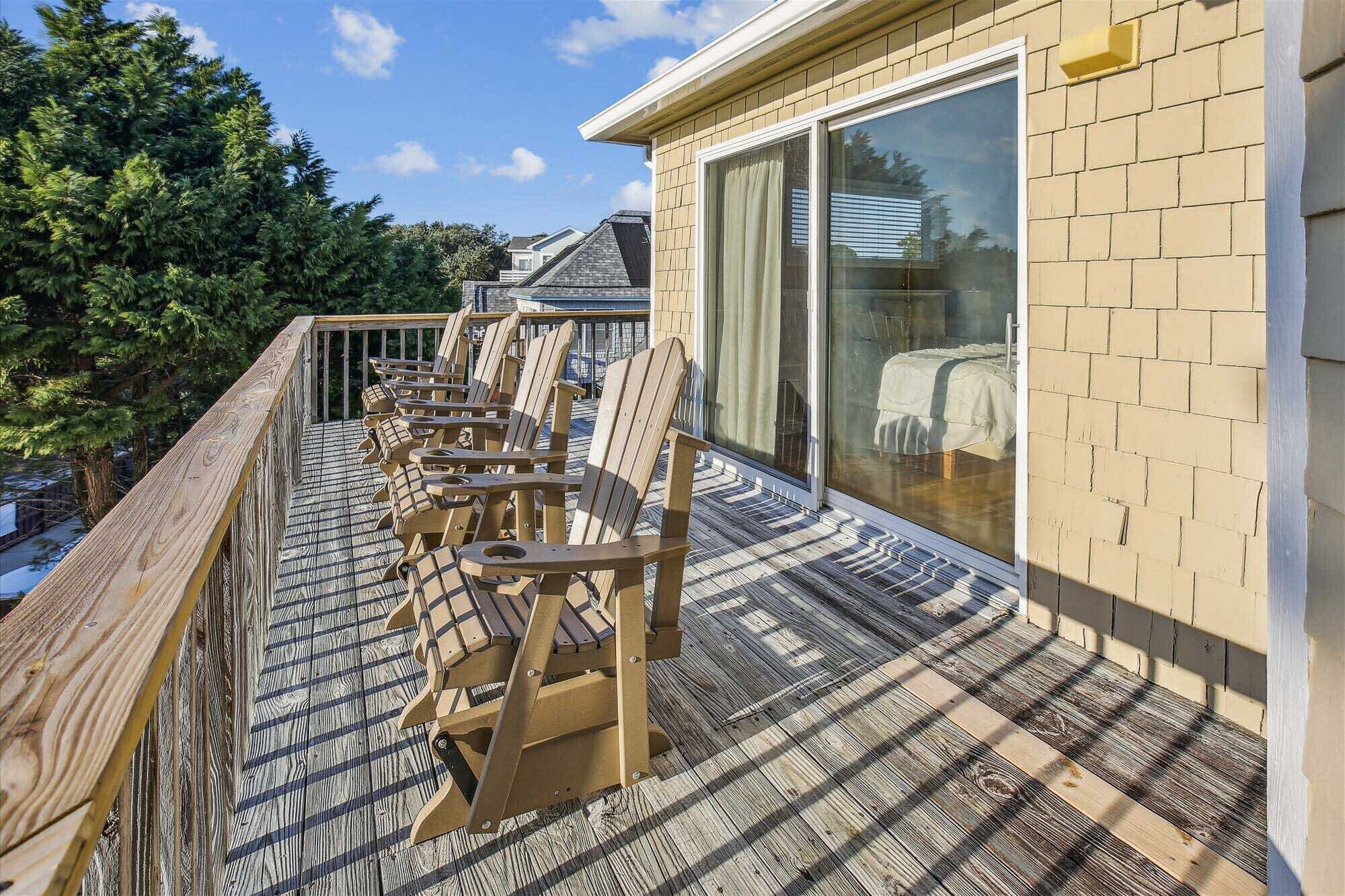 A deck with wooden chairs and a glass door leading to a covered area.