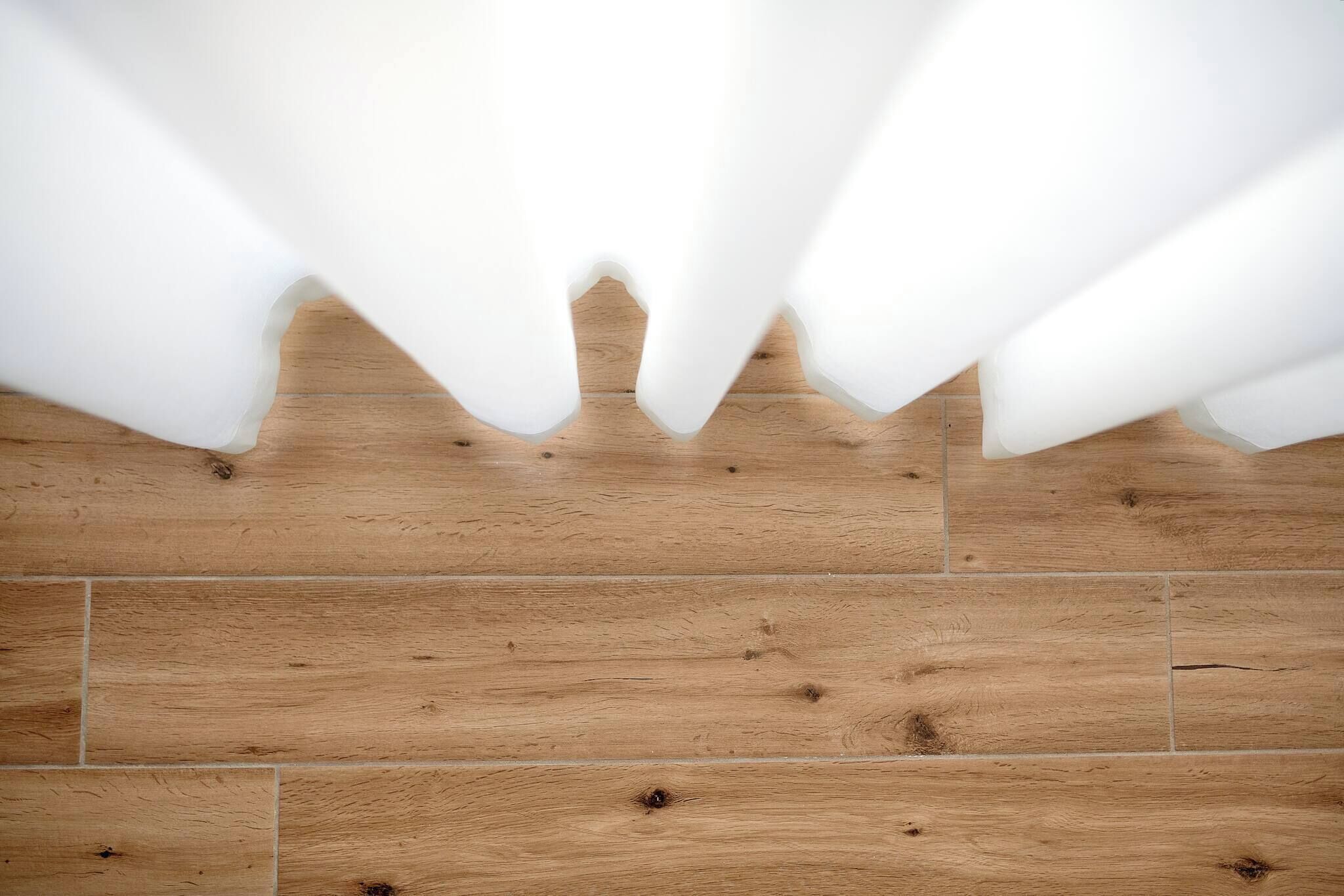 A wooden floor with white curtains partially drawn.