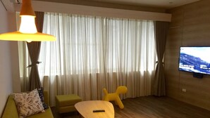 A modern living room with a sofa, a small table, a TV, and a large window with curtains.