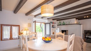 A dining area with a round table, chairs, a fruit bowl, and a hanging light fixture.