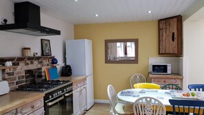 Une cuisine compacte équipée d’une cuisinière à gaz, d’un four et d’un four à micro-ondes. On y trouve une table à manger avec des chaises et une petite fenêtre au-dessus.