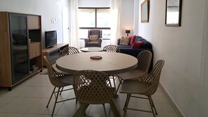 Un salon comprenant une table ronde, quatre chaises, un canapé, un téléviseur et un meuble.