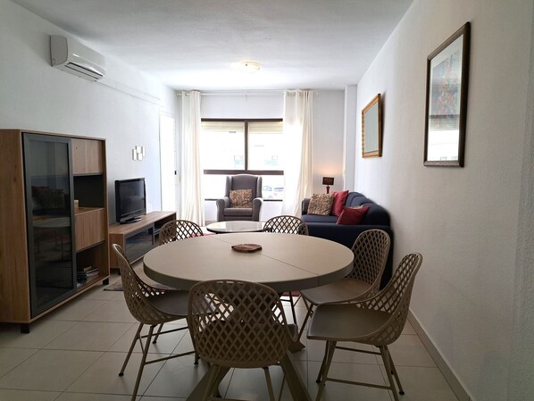 A living room with a round table, four chairs, a sofa, a TV, and a cabinet.