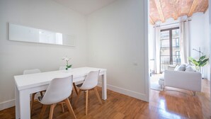 Uma sala de estar moderna com um sofá branco, uma mesa de jantar com cadeiras e uma grande janela com cortinas.