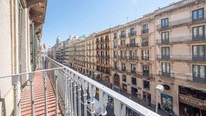 Uma fileira de edifícios históricos com varandas, uma rua para pedestres e um céu azul límpido.