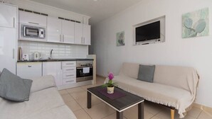 Une cuisine moderne avec des meubles blancs, un four à micro-ondes et une cuisinière. On y trouve un canapé avec un coussin et une petite table sur laquelle est posée une plante.