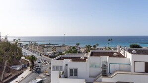 Un quartier résidentiel en bord de mer, avec des bâtiments blancs, une route bordée de voitures garées et une vue sur la mer.