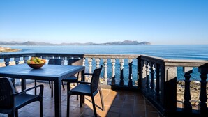 Una terraza con una mesa y sillas, un frutero y vistas al mar y montañas a lo lejos.