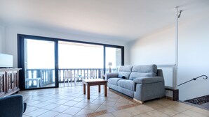 Un balcón amplio con puerta corrediza de vidrio, un sofá gris, una pequeña mesa de madera y un sillón azul.