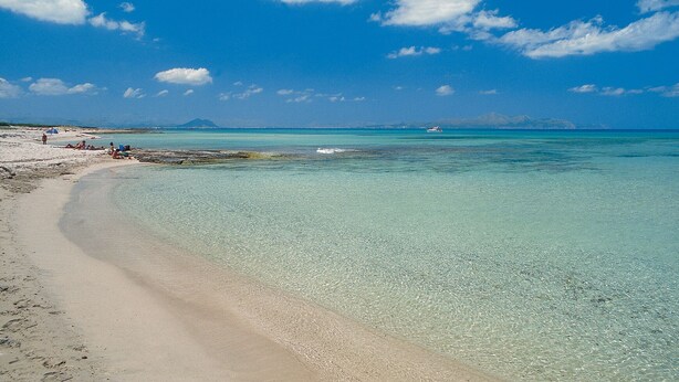 Una playa con agua turquesa cristalina, una orilla arenosa y una montaña distante.