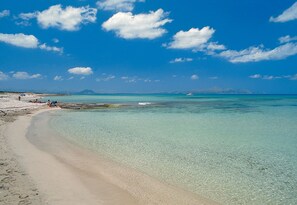 Una playa con agua turquesa cristalina, una orilla arenosa y una montaña distante.