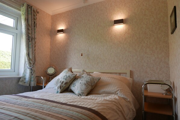 A neatly made bed with a striped bedspread, a bedside table with a mirror, and a wall-mounted shelf.