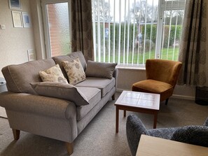 A living room with a grey sofa, a brown armchair, and a small table. - 35 Siesta Mar -  a holiday chalet that sleeps 4 guests  in 2 bedrooms (Norwich)