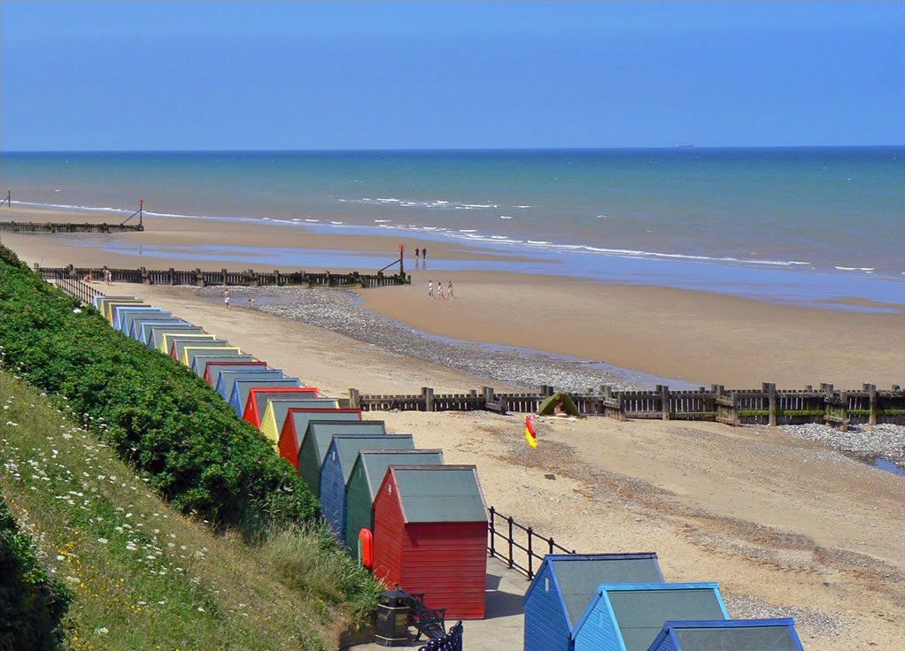 A beach with colorful beach huts and a wooden pier.