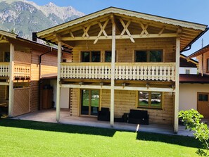 A wooden chalet with a balcony, large windows, and a view of mountains.