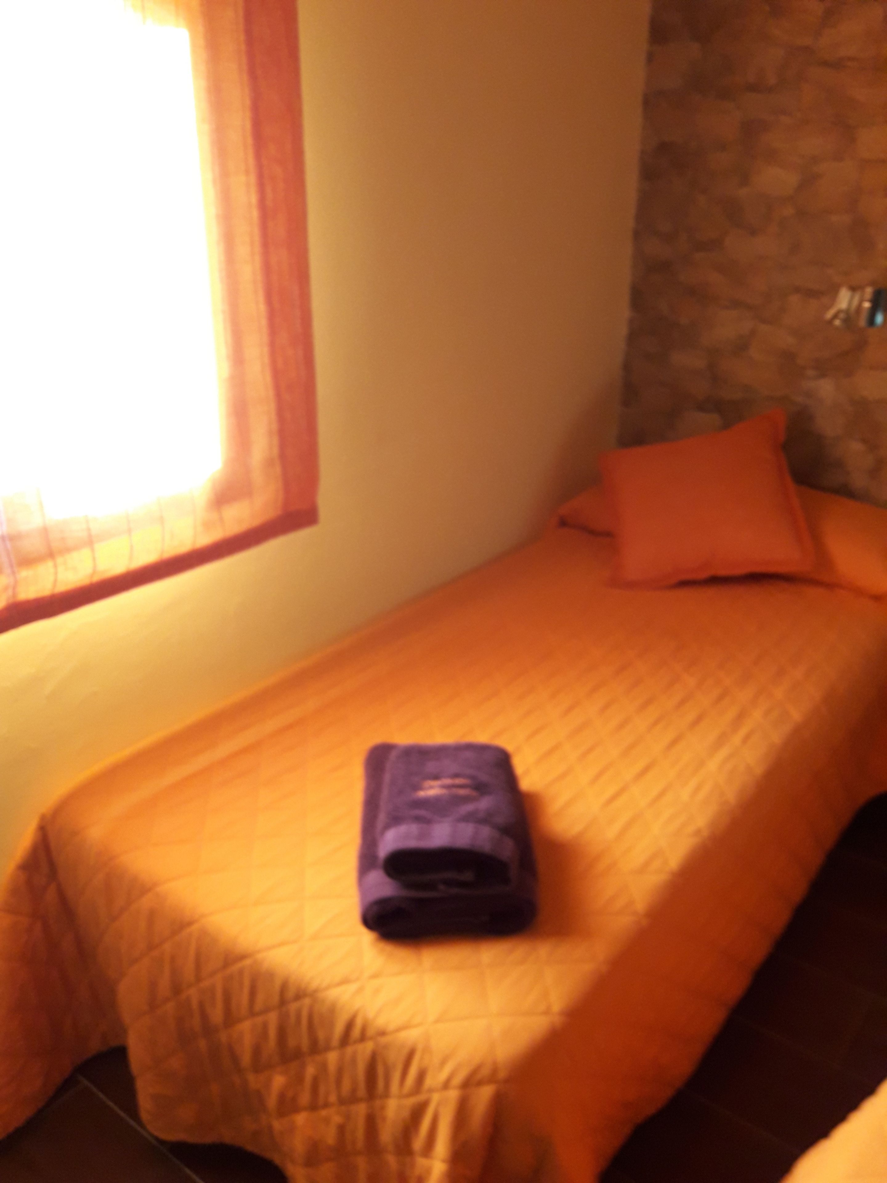 Un lit simple avec une couvre-lit orange et une serviette violette pliée posée dessus.