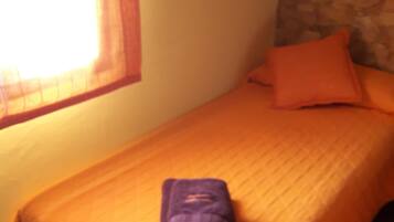 Un lit simple avec une couvre-lit orange et une serviette violette pliée posée dessus.