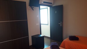 Une chambre d’hôtel avec deux lits, une armoire, un téléviseur fixé au mur et une porte donnant sur l’extérieur.